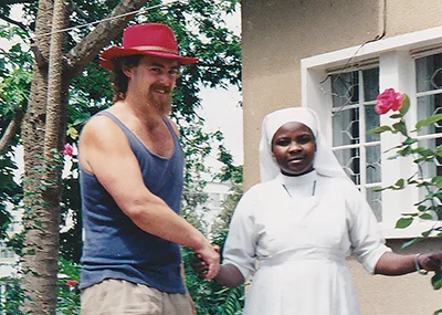 Man wearing a red hat and blue singlet shaking hands with an African nun